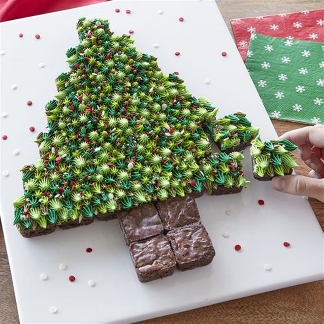 وزعي البراونيز بالشوكولاته على صينية بيضاء وبشكل شجرة الميلاد وزينيها بالكريما الخضراء وبعض الحبيبات الملونة.