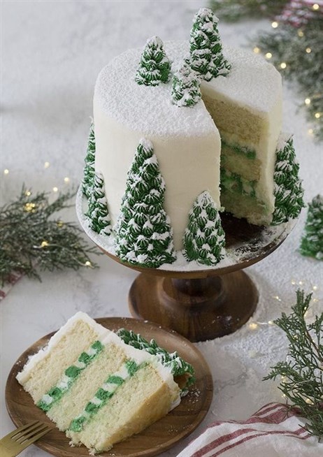 زيني قالب الحلوى لتقديمه على العشاء أو الغداء بالكريما البيضاء واشكال الاشجار الخضراء المغطاة بالثلج.