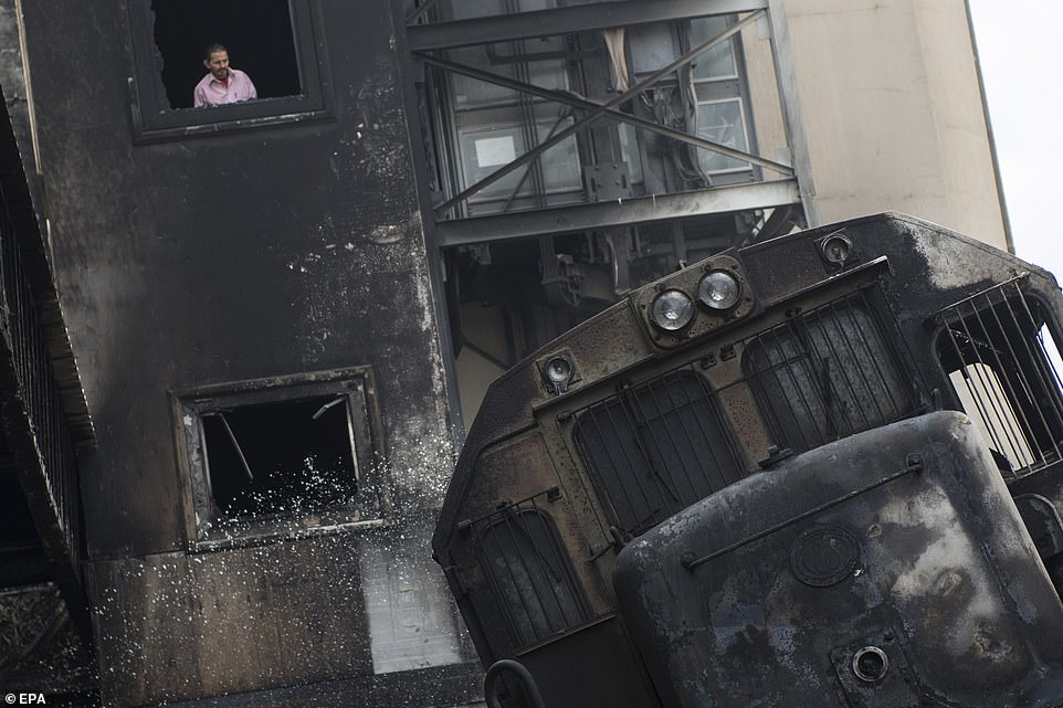 A man looks out from a window towards a burnt-out train on tracks after a fire broke out at the main train station in Cairo