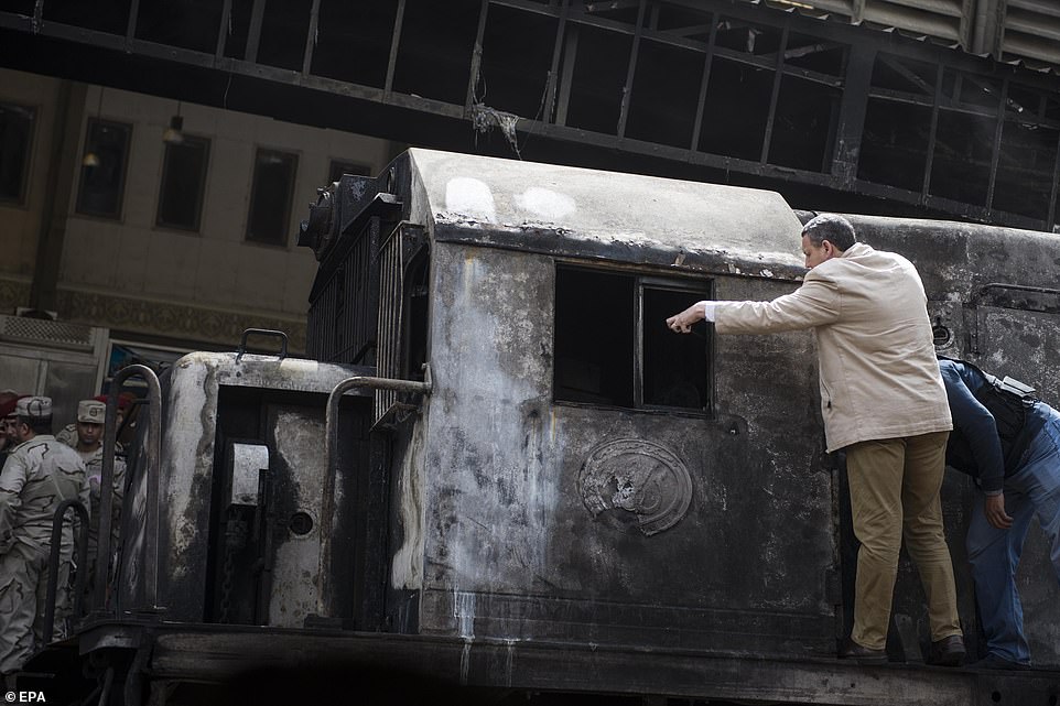 Officials inspect a burnt-out train engine on tracks after a fire broke out at the main train station in Cairo