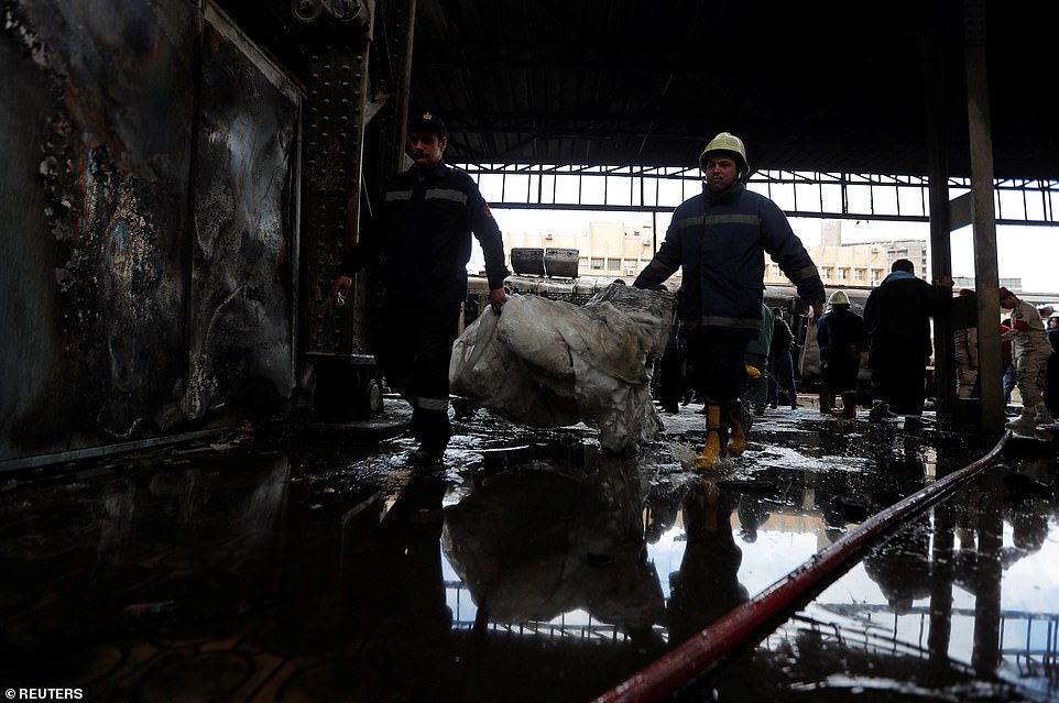 A member of security forces and a rescue worker carry away charred packing material after a crash at Cairo's main station