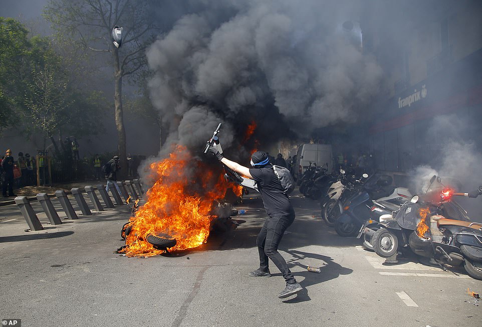 A protestor throws a scooter onto a pile of burning motorbikes during a yellow vest demonstration in Paris, today