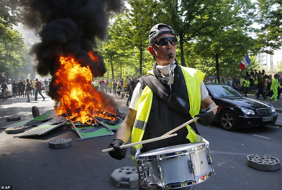 A man bangs a drum in front of a fire on the street during a yellow vest demonstration in Paris