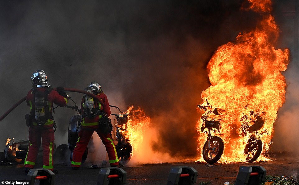 Firefighters battle blazing scooters in a Paris street by spraying them with water as demonstrations raged in the capital city