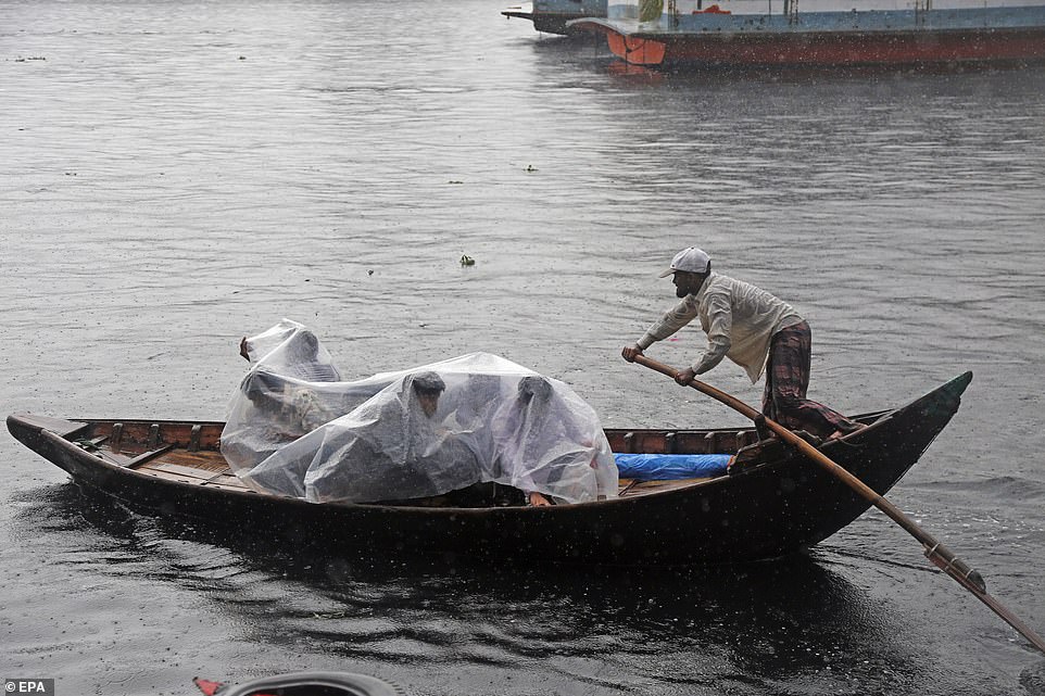 Bangladeshi passengers cover themselves with a plastic sheet as they cross the Buriganga River by boat during a rainy day in Dhaka
