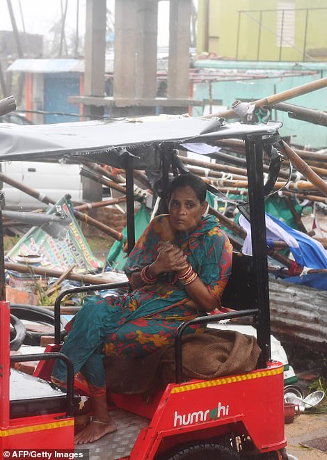 An Indian resident sits on an electric rickshaw next to a damaged structure