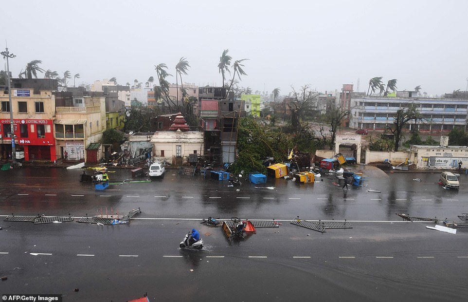 Indian residents ride along a road next to damaged trees. The storm sent coconut trees flying, blew away food stands and cut off power and water