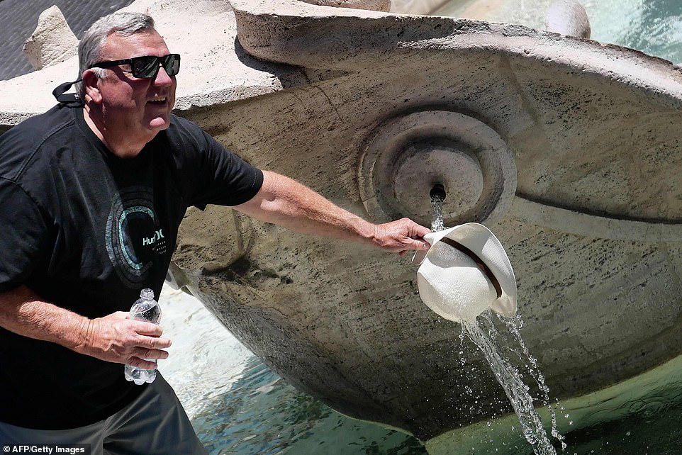 A man wets his hat at a public fountain during an unusually early summer heatwave on June 24, 2019 in Rome