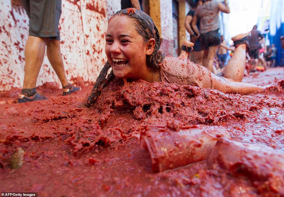A smiling and clearly delighted young woman dives into a thick pile of tomato pulp during this year's edition of the annual festival