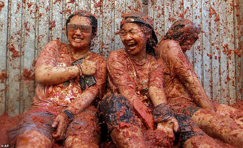 A group of friends smeared in tomato pulp sit against the wall as they are hit with a barrage of tomatoes during the festival