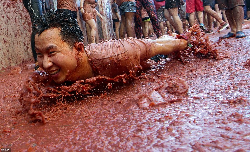 A delighted reveller slides along the ground during the festival, covering his front in a huge pile of tomato pulp at the event