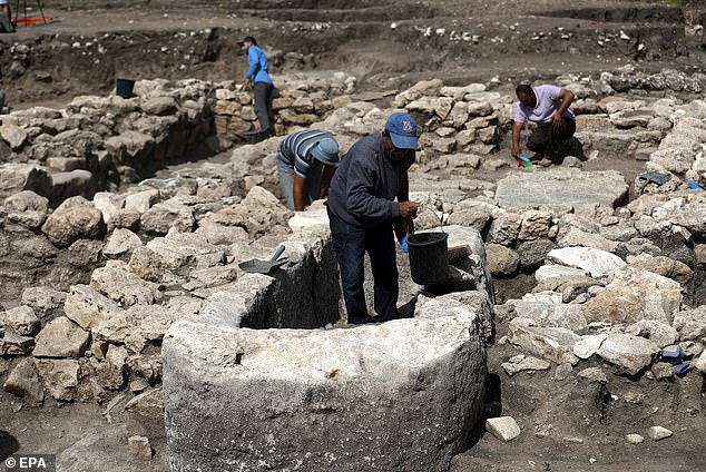Israeli employees of the Israel Antiquities Authority (IAA) work on a stone basin for liquids, apparently used for religious rituals, at the site of the 5,000-year-old city