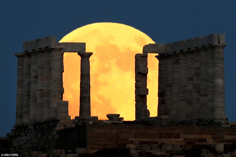 Stunning: The Blood Moon smoulders an orange-yellow as it rises behind the Temple of Poseidon during the lunar eclipse 