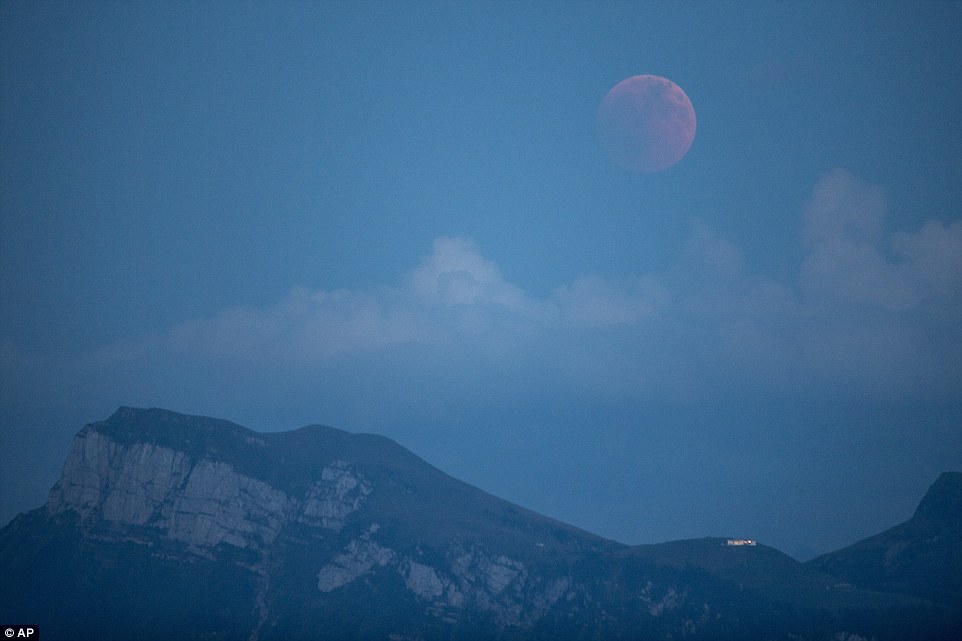 Switzerland: The red moon starts to show above the mountains in Lucerne as night falls across Europe 