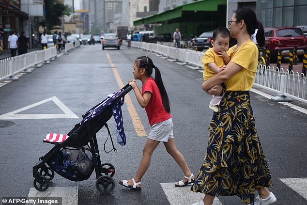 A girl pushes a pram through Beijing while a woman follows behind carrying a baby in July 2018
