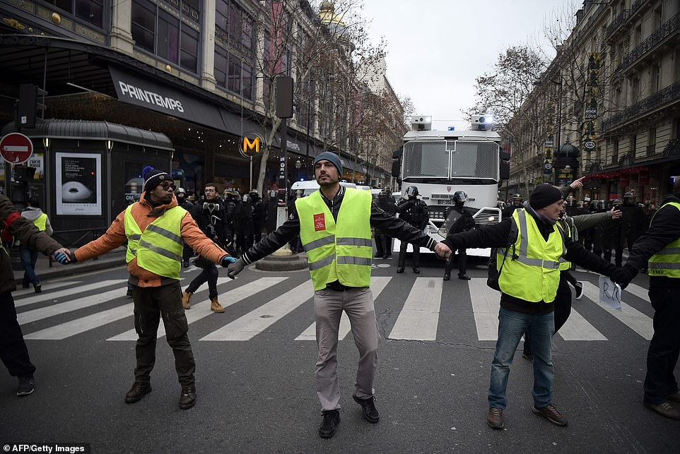 Protestors are seen holding hands across a street in front of a line of security personnel in Paris today. The latest opinion poll, published on Thursday by Odoxa Dentsu, indicated 55 percent public support for the 'yellow vest' protests