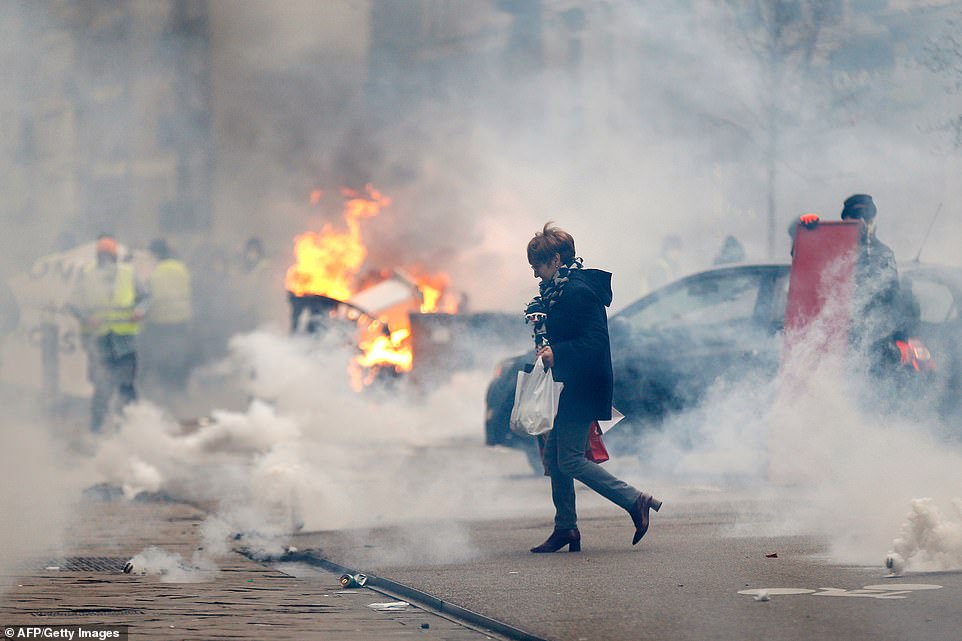 A woman walks through smoke passing burning material during a rally by yellow Vest anti-government protesters in Rouen. This is the eighth Saturday of protests called by the grass-roots movement