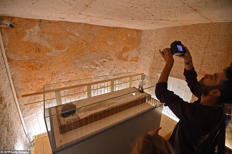 A man uses a camera to take a picture of the linen-wrapped mummy of the 18th dynasty Pharaoh in his underground tomb